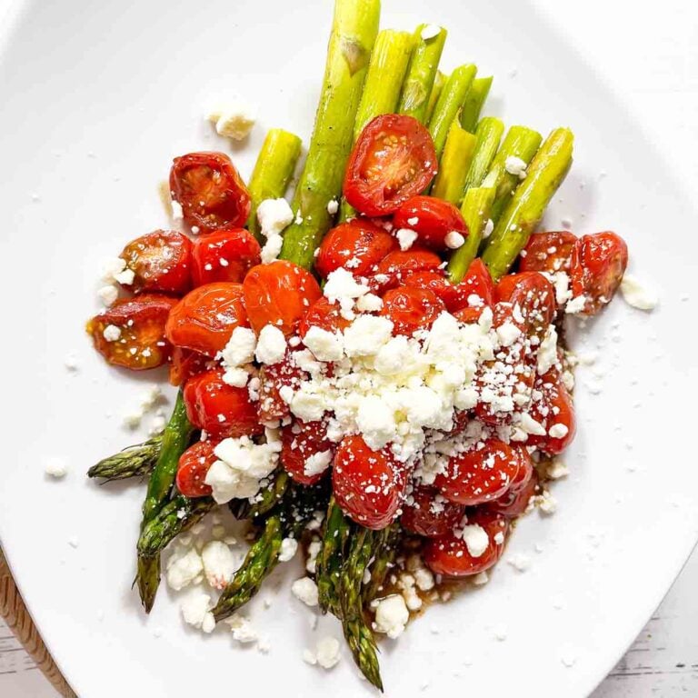 roasted asparagus and cherry tomatoes with feta on a white plate.