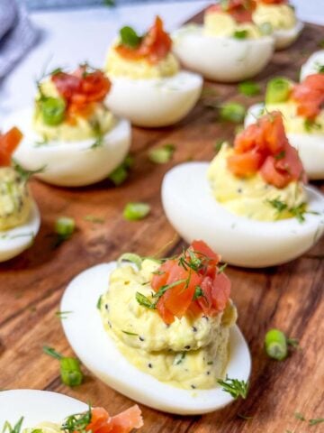 everything bagel deviled eggs with cream cheese and smoked salmon on a wooden board.
