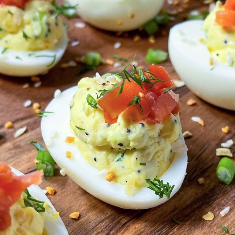 everything bagel deviled eggs with cream cheese and smoked salmon on a wooden board.