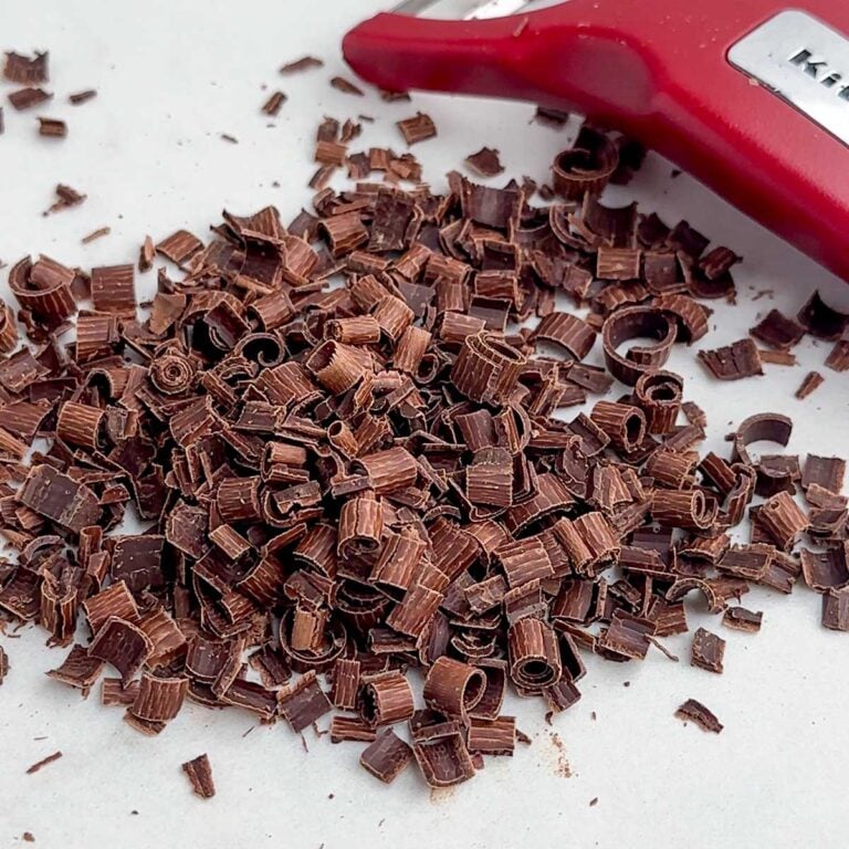a pile of chocolate curls next to a vegetable peeler.