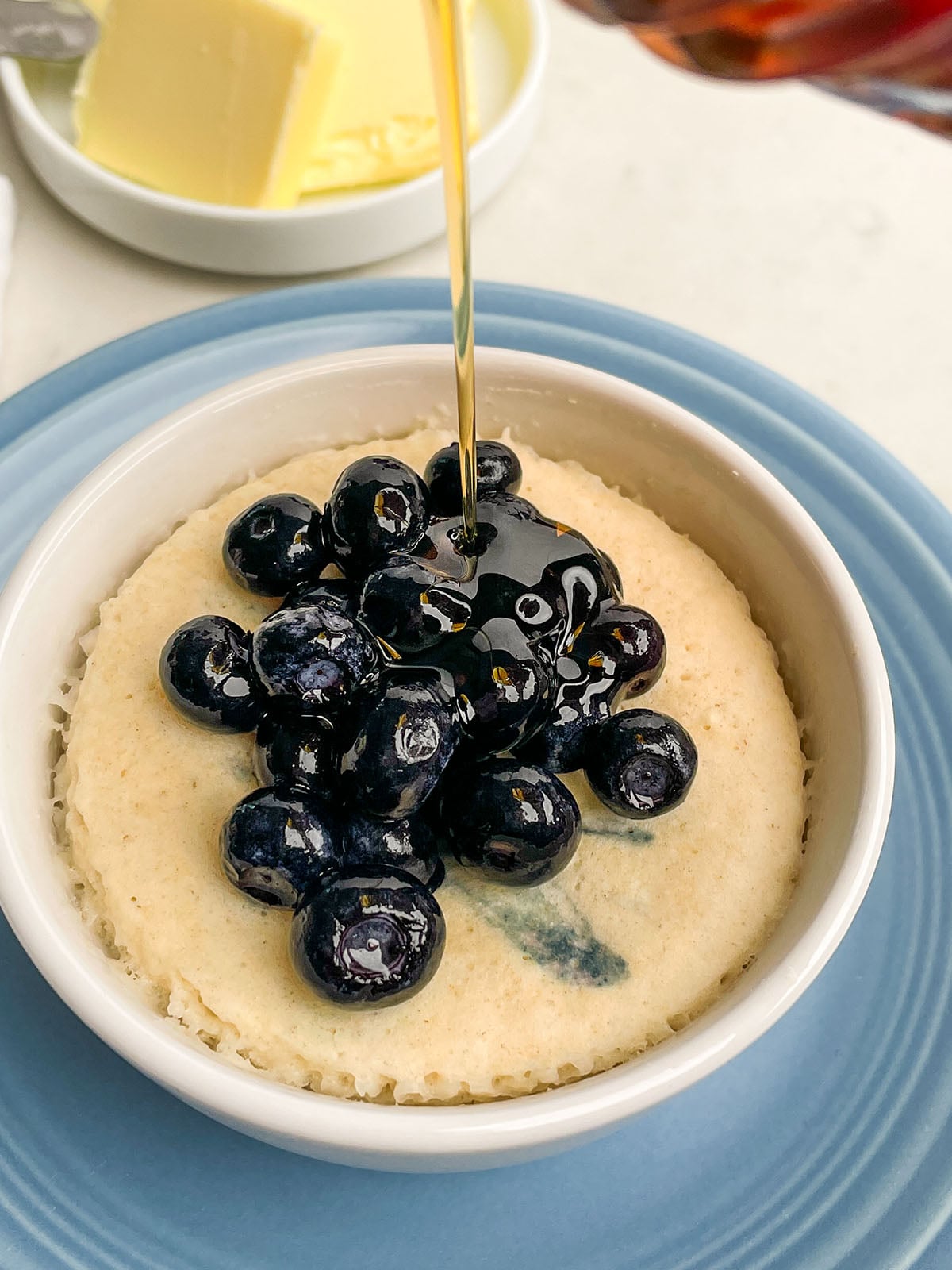 blueberry pancake in a mug topped with blueberries and maple syrup.