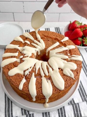 spoon drizzling cream cheese glaze over strawberry angel food cake.