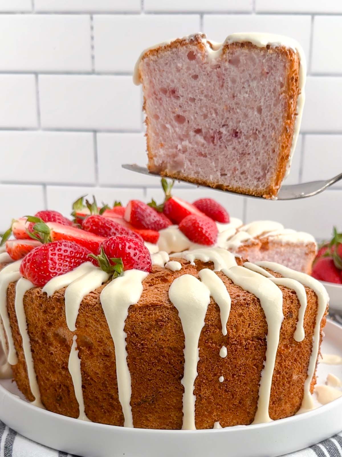 cake server holding a piece of strawberry angel food cake above the cake on a plate.