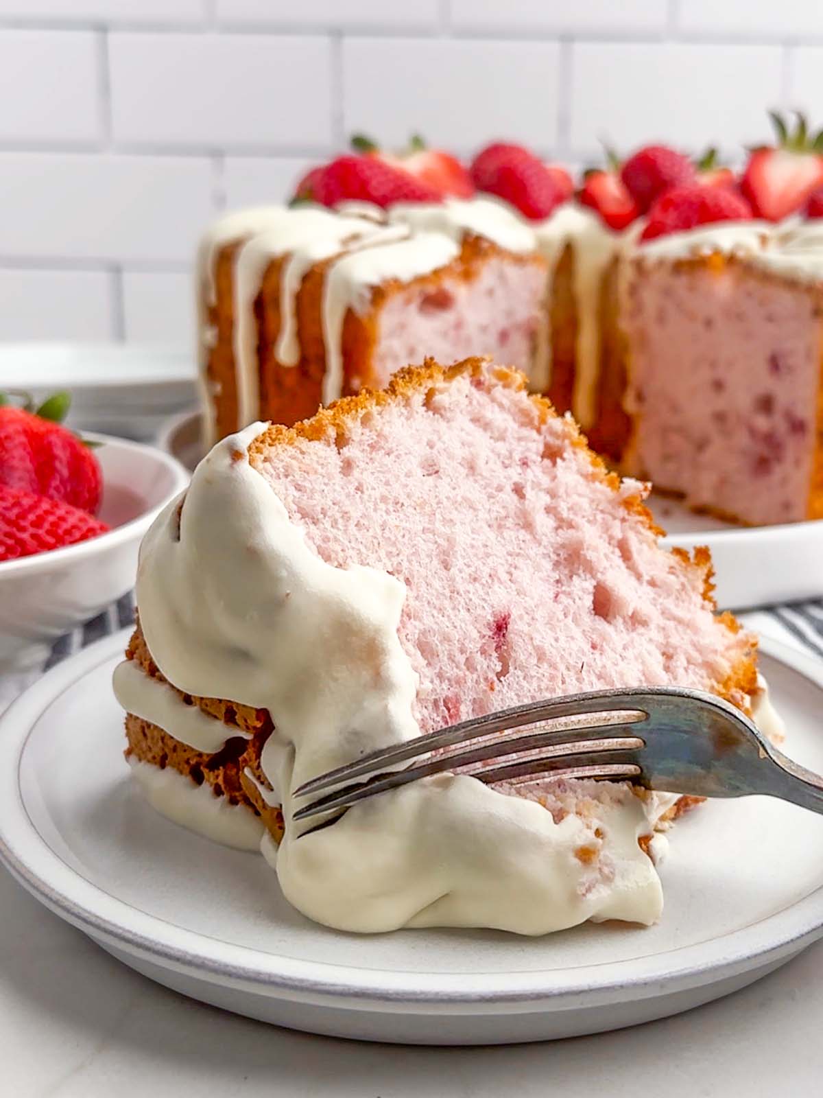 cake server lifting a piece of strawberry angel food cake from the cake on a plate.