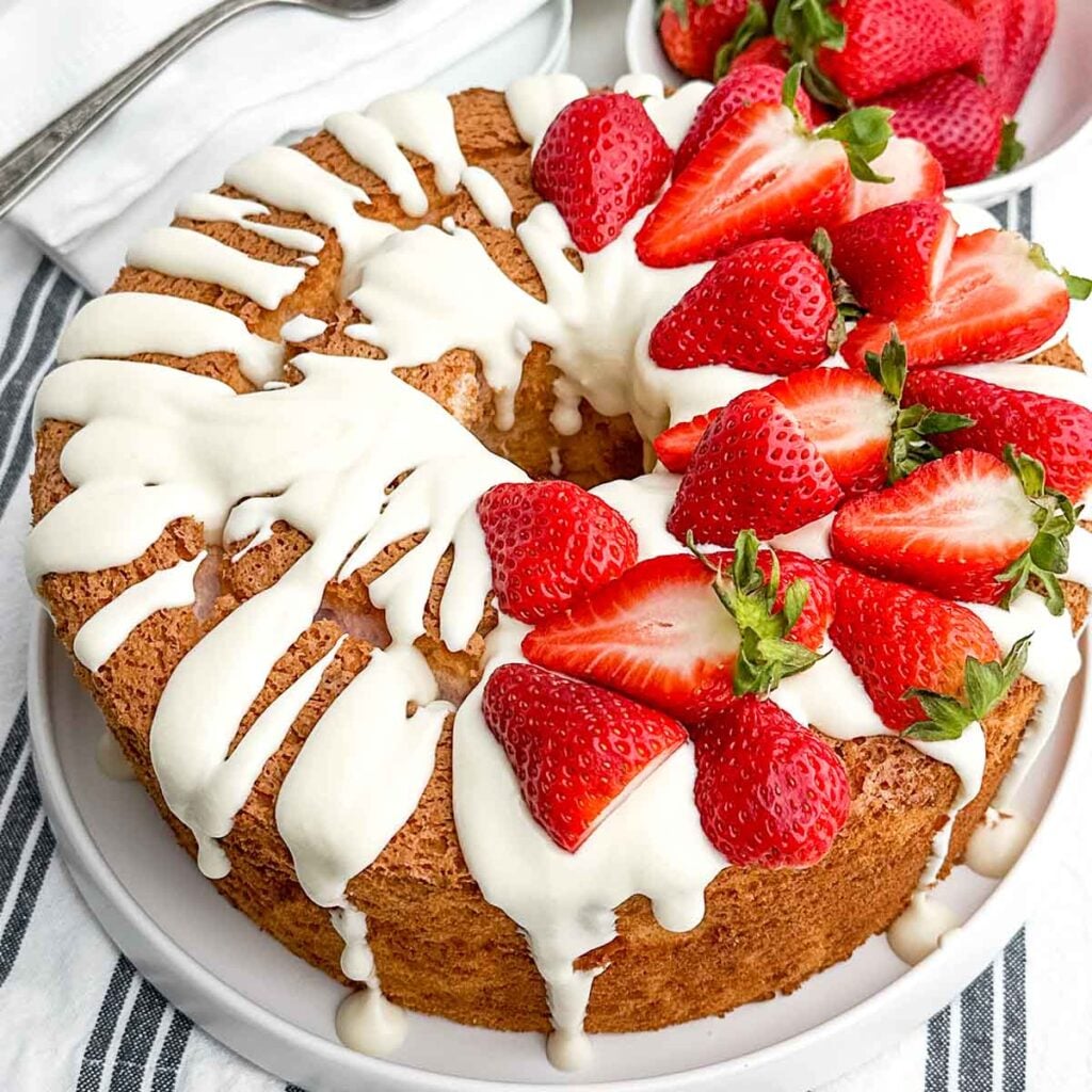 strawberry angel food cake topped with cream cheese glaze and fresh strawberries.