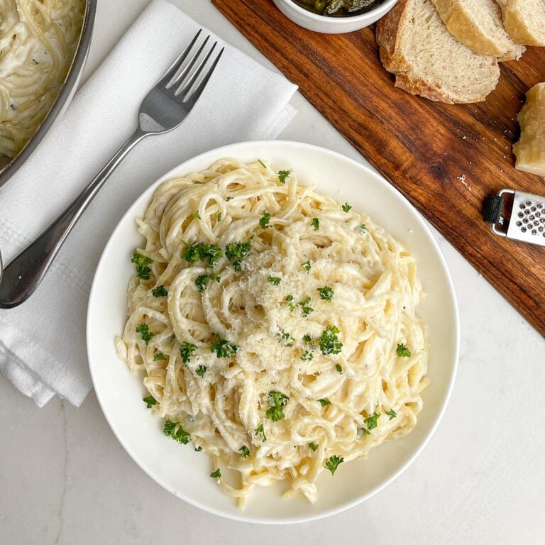 plate of spaghetti with alfredo sauce on white counter next to napkin and fork