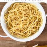 a colander of cooked spaghetti with a bundle of dry spaghetti on a wooden cutting board.