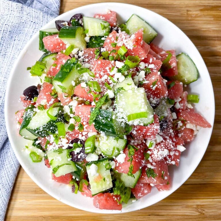 watermelon goat cheese salad in a white bowl on a wooden cutting board.
