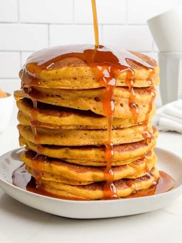 pumpkin syrup being poured onto pumpkin pancakes