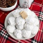 Mexican Christmas cookies on a white plate next to a holiday mug and bowl of pine cones