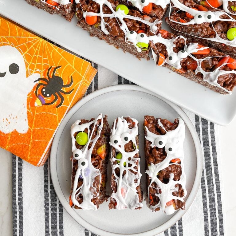 Halloween rice krispie treats on a white plate with a platter of treats in background
