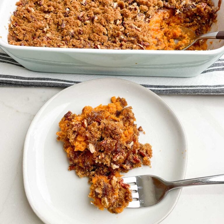 white plate with a serving of Paula Deen sweet potato casserole next to white casserole dish