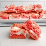 two Strawberry Brownies ona white plate in front of a platter of strawberry brownies