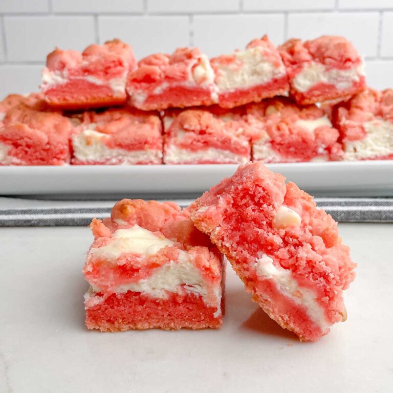 two Strawberry Brownies ona white plate in front of a platter of strawberry brownies