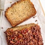 slice of chocolate chip pecan banana bread next to a cut loaf on white parchment papaer.