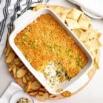 crab spinach artichoke dip in white baking dish with pita chips and crostini