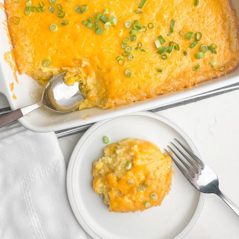 Paula Deen Corn Casserole in a white casserole dish next to a plate of one serving of corn casserole