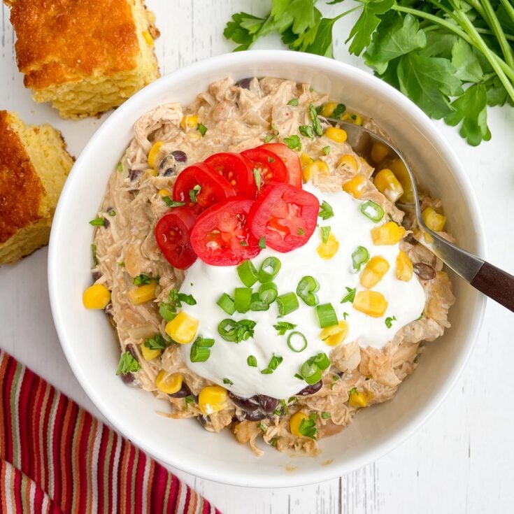 cream cheese chicken chili in a white bowl with cornbread and parsley on a white countertop