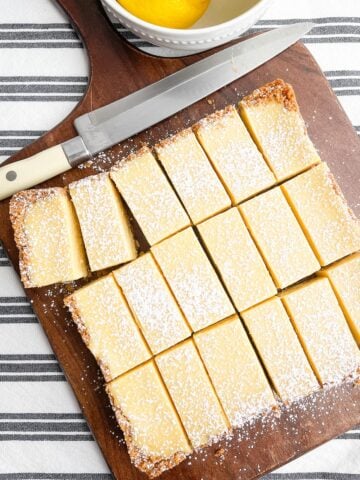 lemon bars with graham cracker crust on cutting board with a knife on black and white napkin