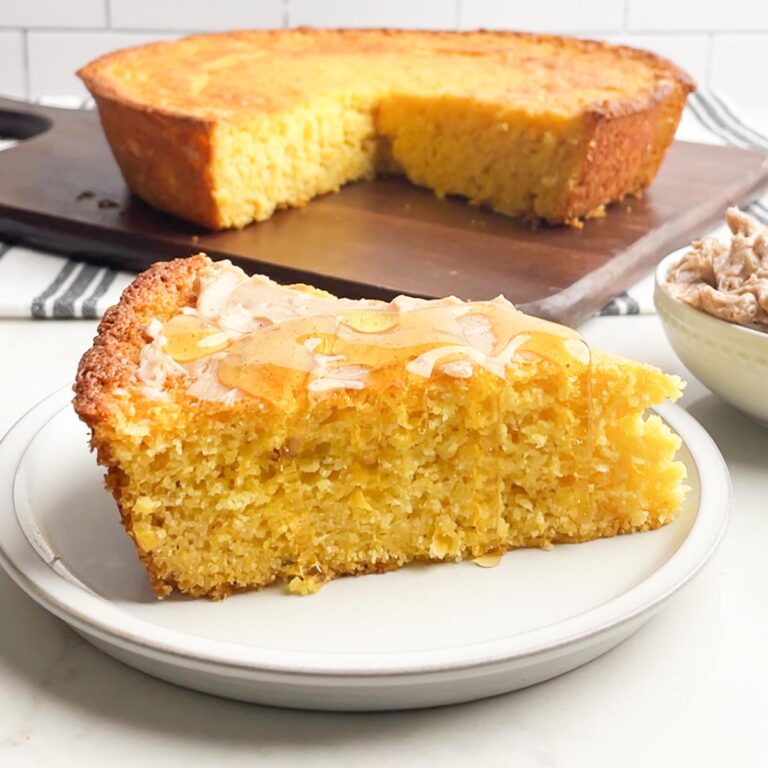piece of Jiffy sweet corn bread on white plate topped with cinnamon honey butter and honey