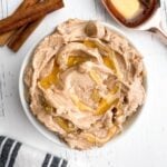 Texas Roadhouse butter in white bowl with cinnamon sticks and tablespoon of honey on white wooden countertop