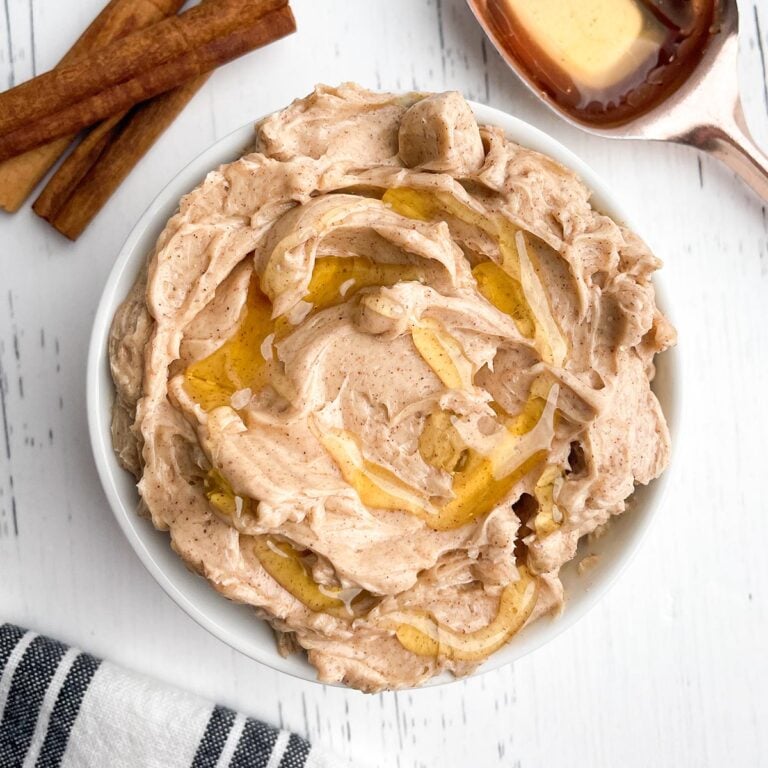 Texas Roadhouse butter in white bowl with cinnamon sticks and tablespoon of honey on white wooden countertop