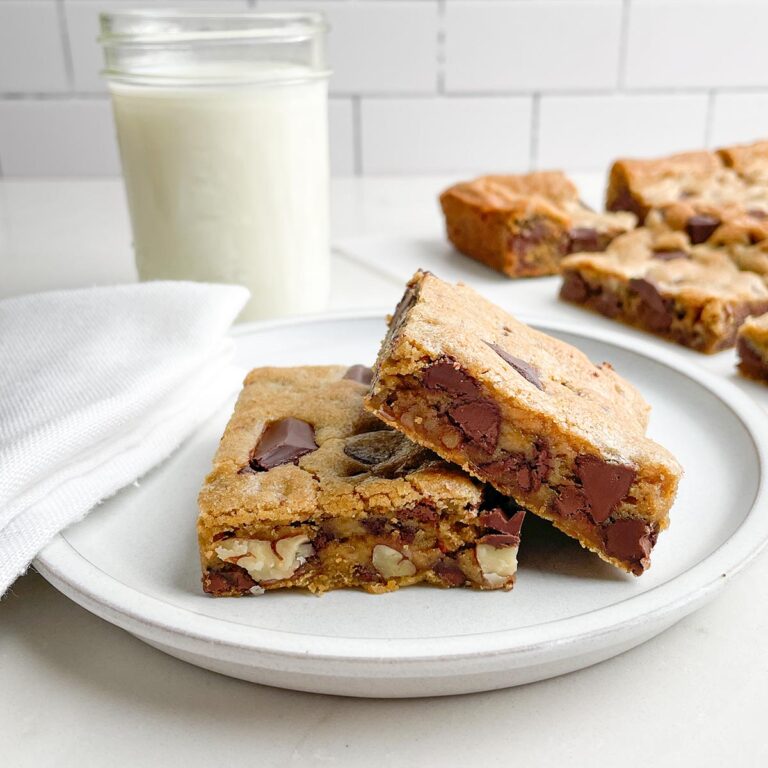 Toll House cookie bars on a white plate with bars and a glass of milk in background