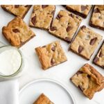 toll house cookie bars on a white countertop next to a glass of milk.