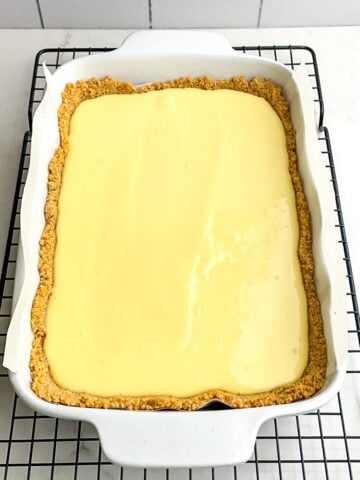 unbaked lemon bars with graham cracker crust in white baking pan on wire rack