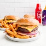 air fryer cheeseburger and french fries on a white plate with plates of hamburgers and fries in background