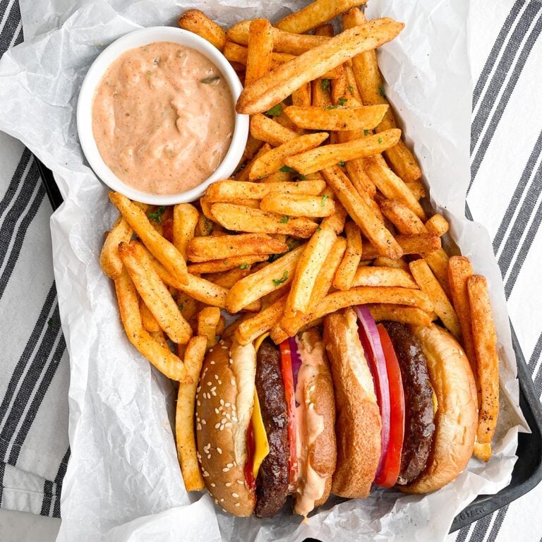 air fryer frozen hamburger with french fries and dipping sauce in a parchment lined pan