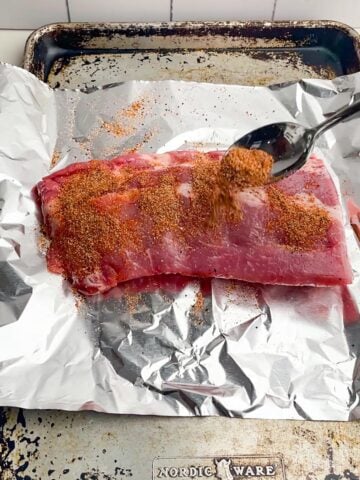 spoon sprinkling dry rub on a rack of ribs set on foil