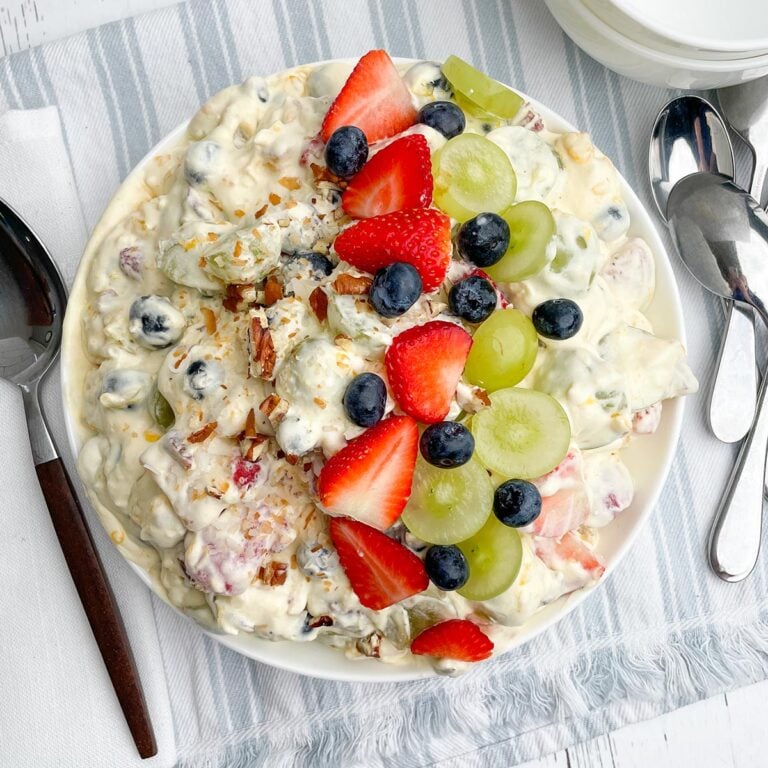 fruit salad recipe with cool whip topped with coconut and pecans and fruit in a white bowl