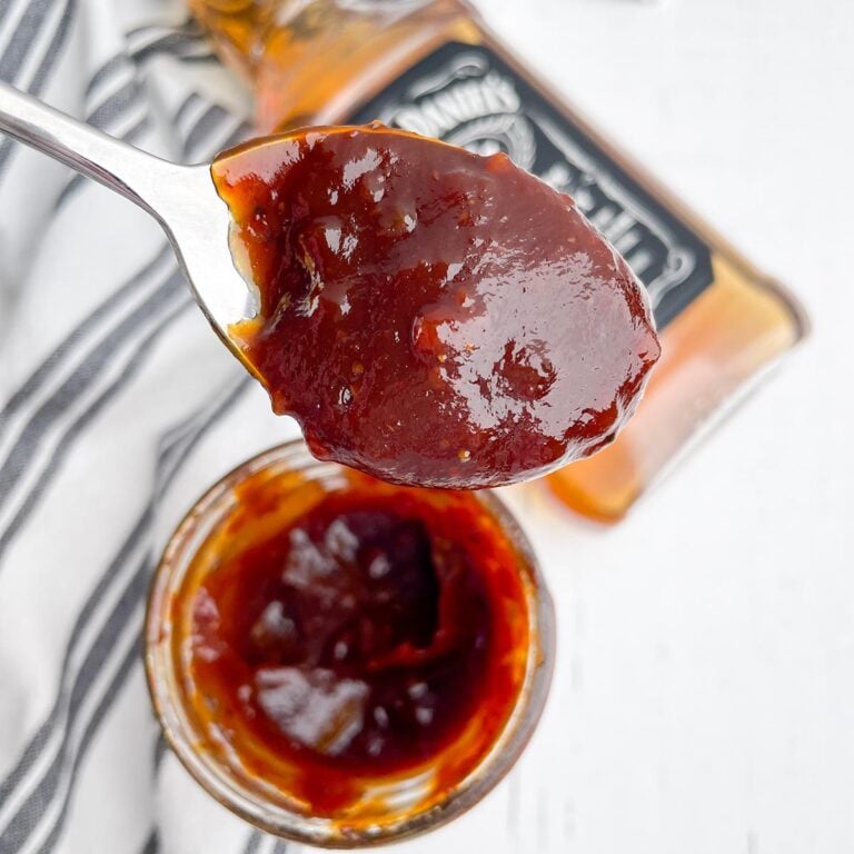 jack daniels bbq sauce in a mason jar with a spoonful of sauce in foreground and bottle of jack daniels in background