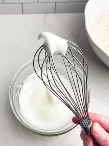 hand holding up a whisk with beaten egg whites