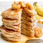 a stack of banana pancakes with caramelized banana topping on a white plate.