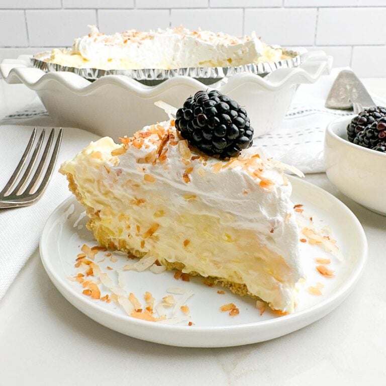 side view of white plate with piece of pineapple cream cheese pie topped with toasted coconut and a blackberry
