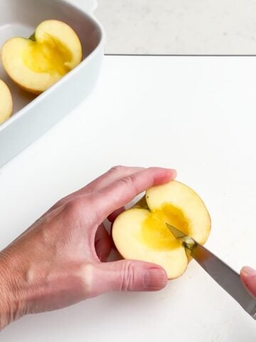hand holding an apple and a paring knife cutting out the blossom end of the apple