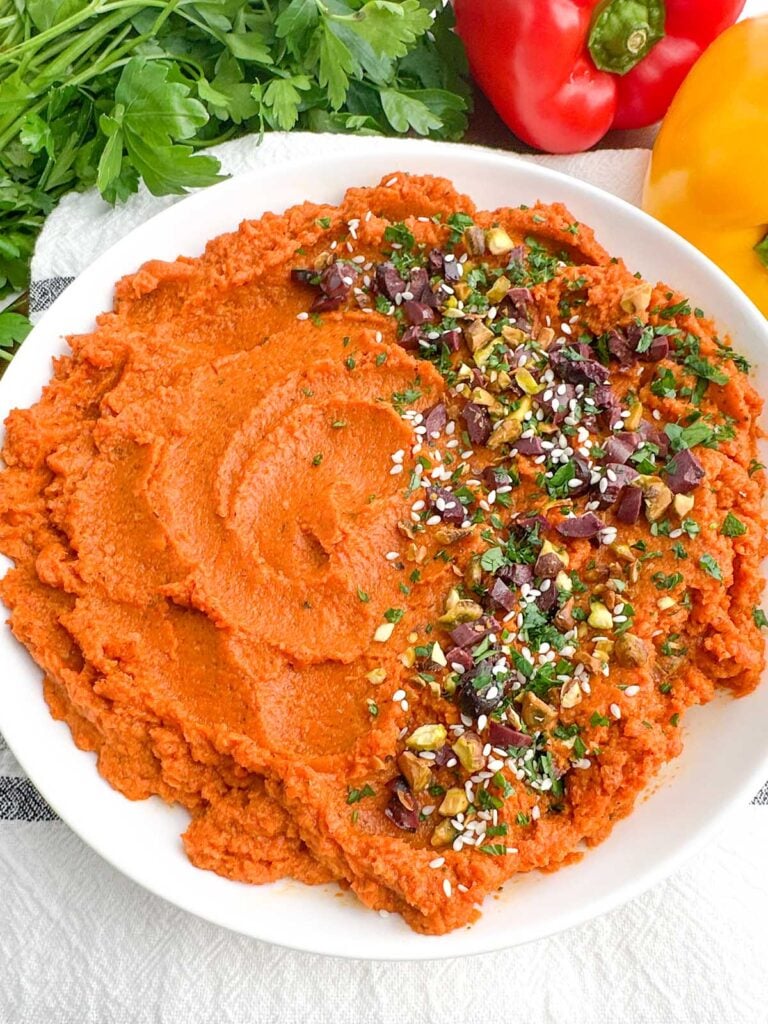 roasted carrot hummus in a white bowl next to fresh bell peppers and parsley.