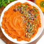roasted carrot hummus in a white bowl next to fresh bell peppers and parsley.