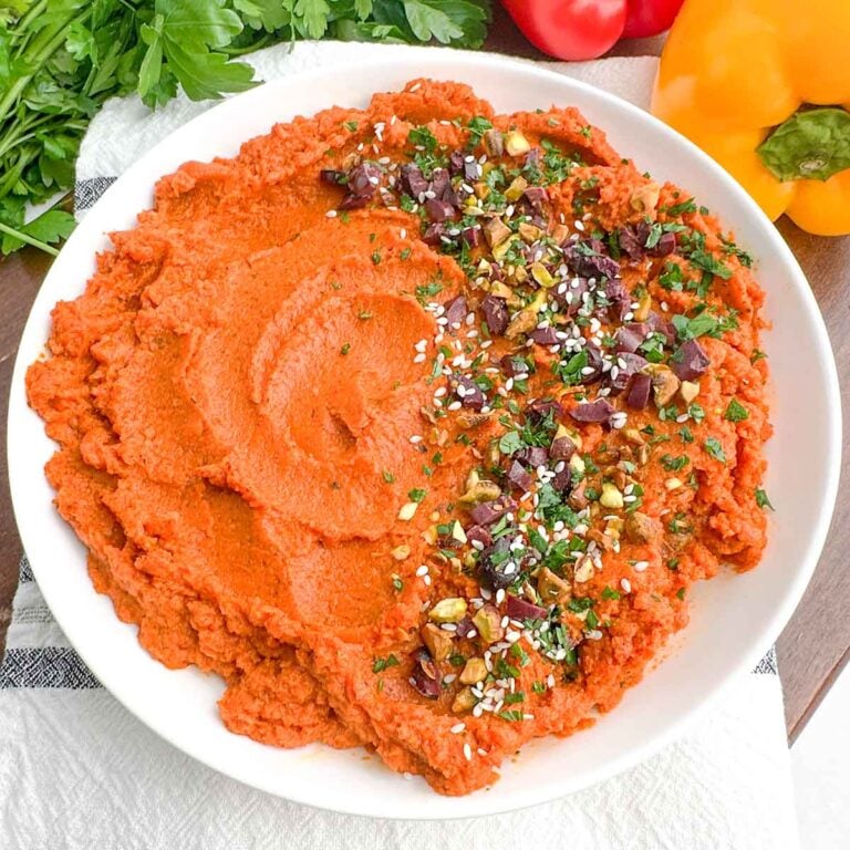roasted carrot hummus in a white bowl next to fresh bell peppers and parsley.