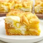 side view of a lemon brownie with cream cheese filling and lemon Oreos on a white plate.