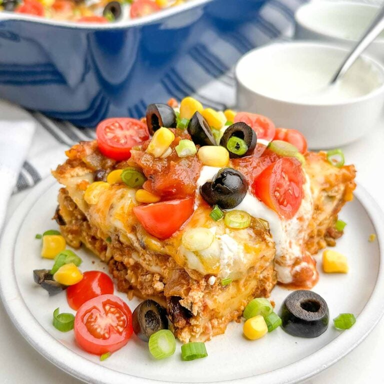 one piece of taco lasagna and taco toppings on a white plate.