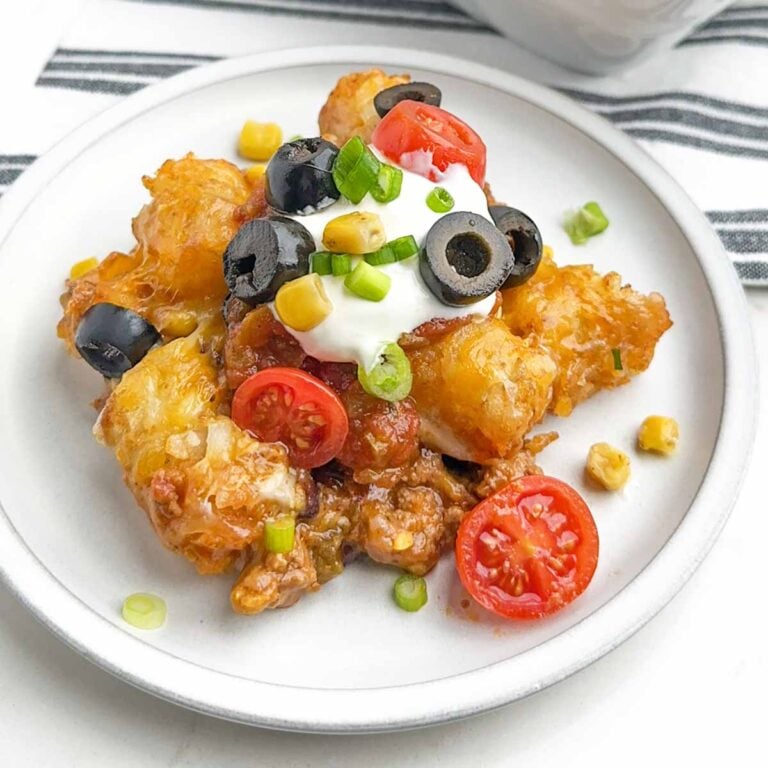 taco tater tot casserole topped with taco toppings on a white plate.