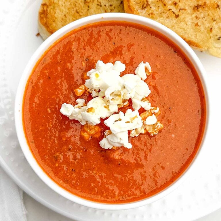 red pepper and gouda soup topped with popcorn in a white bowl with toasted bread on the side.