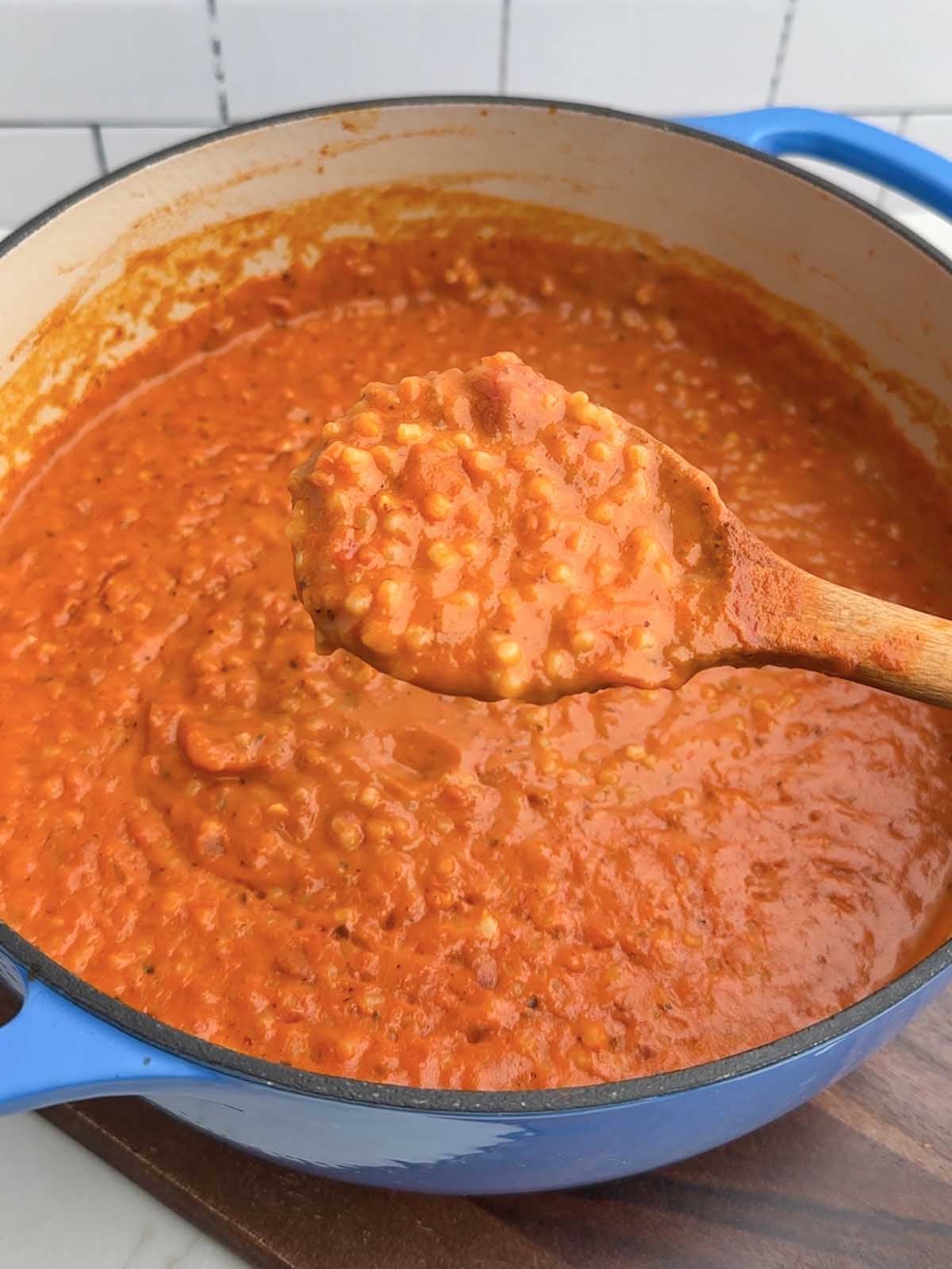 tomato pastina in a Dutch oven with a wooden spoon holding up a spoonful.