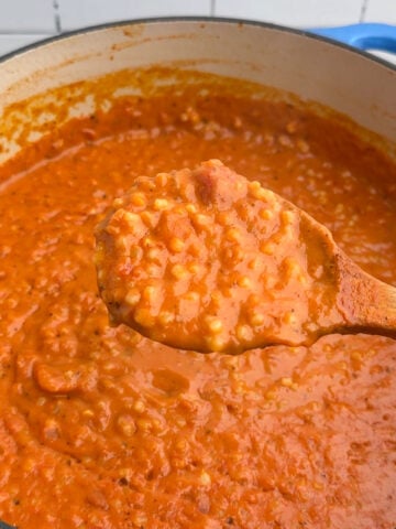 wooden spoon filled with tomato pastina above a Dutch oven.