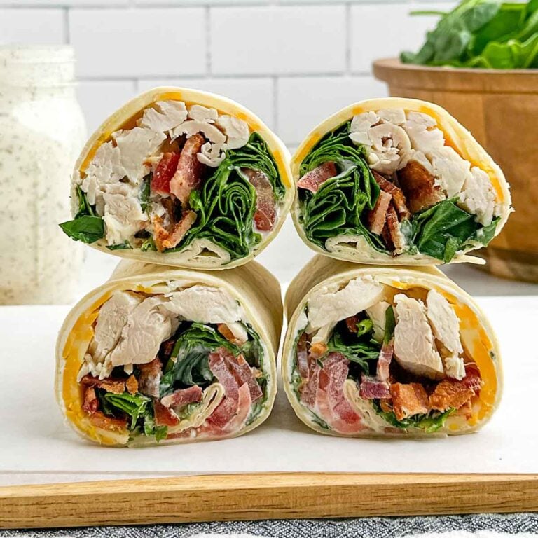 chicken bacon ranch wraps stacked on a wooden cutting board.