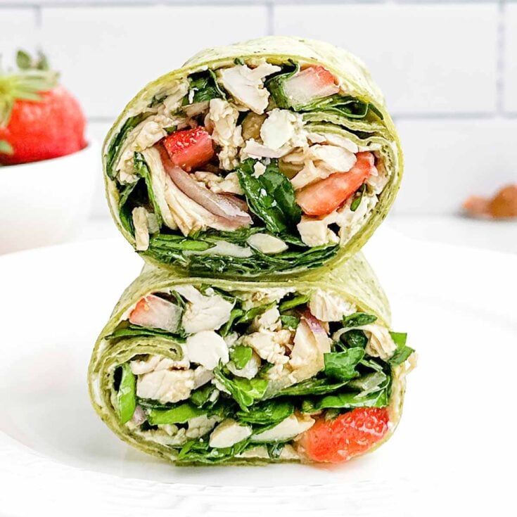 two halves of a chicken spinach wrap on a white plate.