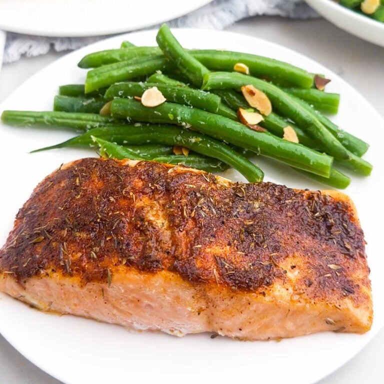 blackened baked salmon filet and green beans on a white plate.